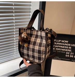 Detail of plaid canvas tote bag with brown straps and a plush bear keychain