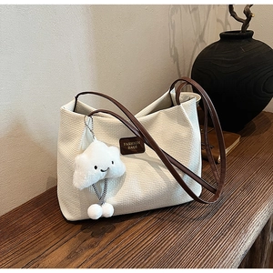 Dettaglio della borsa tote in velluto a coste crema con cinturini marroni e charm