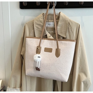 Detail view of cream tote bag with embossed cartoon patterns and plush charm on trench coat