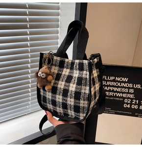 Detail of checkered canvas tote bag with decorative plush monster charm and black handles
