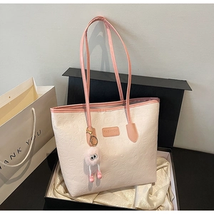 Detail of a cream and pink tote bag with heart embossing and a plush monster charm