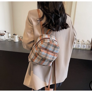 Close-up of a plaid mini backpack with leather straps on a model in a warm cafe