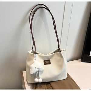 Dettaglio borsa tote beige con texture a nido d'ape, cinturini in pelle e pendente