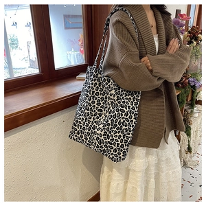 Detailed side view of a large leopard print canvas tote bag worn by a model in a cozy room