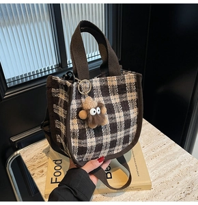 Close-up of brown check fabric handbag with a cute plush monster charm on marble