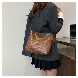 Side view of a brown woven texture shoulder bag worn by a model in professional office setting