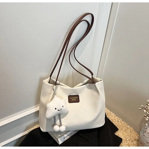 Dettaglio della borsa tote intrecciata crema con manici in pelle marrone e ciondolo nuvola