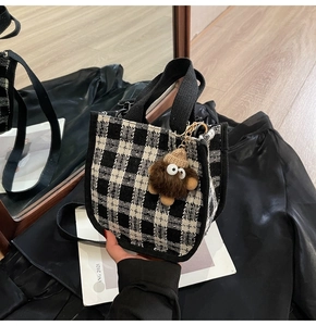 Detail of checkered canvas tote bag with black strap and brown plush monster charm