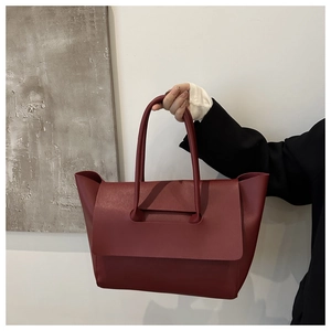 Deep red large capacity tote bag held by hand, showcasing minimalist soft leather design
