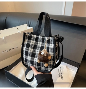 Detail of checkered woven handbag with a cute brown plush monster charm in a gift setting
