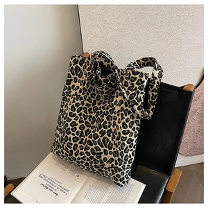 Detail of large leopard print canvas tote bag resting on a black chair with magazine decor