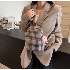 Detail of plaid mini backpack with plush monster pendant against a cafe background