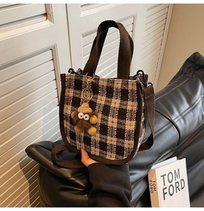 Brown and beige plaid tweed tote bag detail with plush monster charm on black sofa