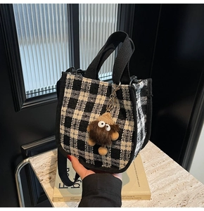 Detail of checkered tote bag with black strap handles and brown plush monster charm