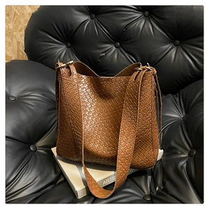Detail of brown leather woven tote bag showing geometric texture and gold metal buckle