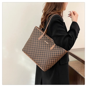 Brown tote bag with letter M monogram pattern shown on shoulder for daily commute