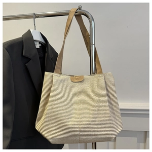 Detail of woven straw tote bag featuring horizontal texture and brown leather straps