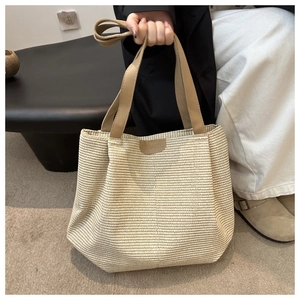 Close-up of woven straw tote bag with brown leather handles and brand label details
