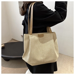 Detail shot of a large woven tote bag with brown leather straps and brand logo patch