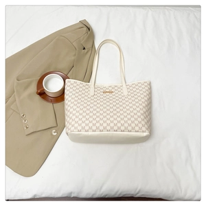 Detail view of cream tote bag with letter print pattern and gold logo plaque