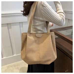 Detail of a large woven tote bag featuring a leather brand tag and long shoulder straps