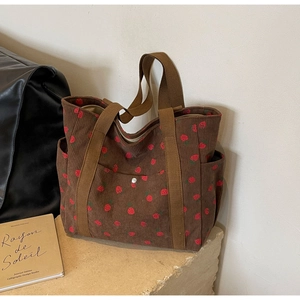 Detail of a brown corduroy tote bag with red strawberry patterns and pocket design