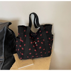 Macro detail of black corduroy tote bag with red strawberry print and side pocket