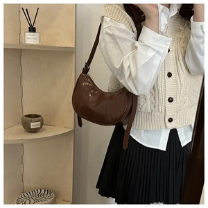 Sac demi-lune en cuir brillant marron dans un décor élégant sur une étagère en bois