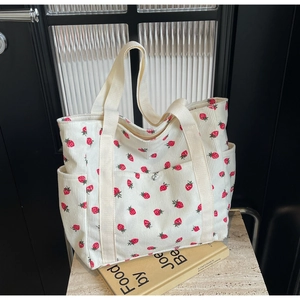 Detailed close-up of a cream corduroy tote bag with red strawberry floral print and pockets