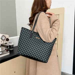 Fashionable black monogram tote bag with gold logo shown in a cozy cafe setting