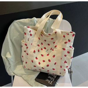 Detail of cream corduroy tote bag featuring red strawberry print and multiple utility pockets