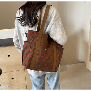 Detailed view of brown corduroy tote bag with strawberry patterns on female model back