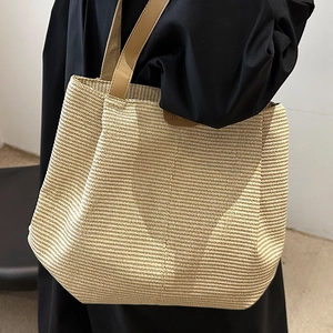Large beige woven tote bag with brown leather handles and brand patch for summer travel