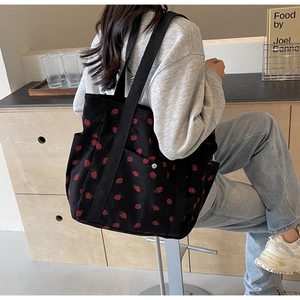 Close-up of black corduroy tote bag with red strawberry pattern and wide shoulder strap