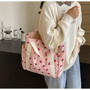 Close-up of pink corduroy tote bag with strawberry prints and cream webbing handles
