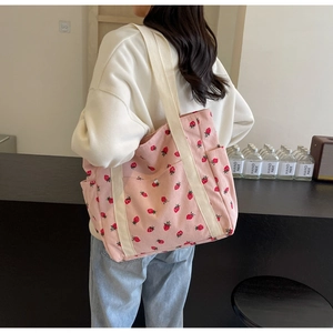 Shoulder view of a pink corduroy tote bag featuring red strawberry prints and wide straps
