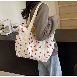 Close-up of white corduroy tote bag featuring red strawberry prints and wide strap