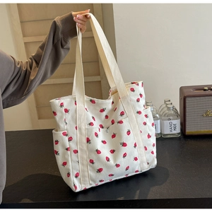 Detail of white corduroy tote bag with strawberry prints and wide webbed handles