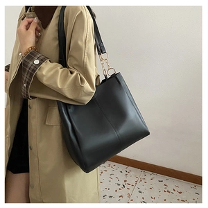 Detail of black leather tote bag featuring gold chain ring hardware and vertical stitching