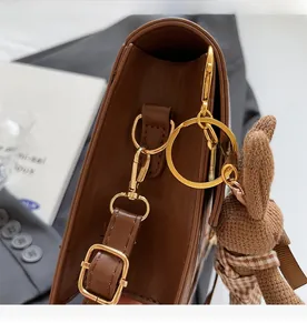 Detail view of brown leather bag showing gold metal hardware and a cute knit bear charm