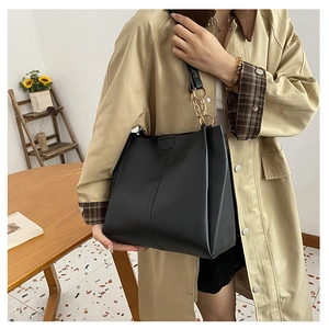 Detail of black faux leather tote bag with gold chain strap on a model wearing a trench coat