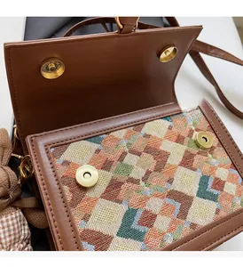 Detail of a brown crossbody bag featuring dual magnetic buckles and textured fabric pattern