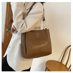 Detail of a brown leather tote bag with vertical stitching and golden chain strap