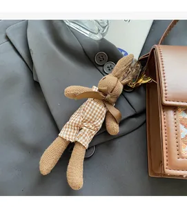 Detailed close-up of a brown knitted rabbit charm with plaid overalls on a leather bag