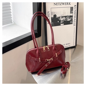 Detail of burgundy glossy leather handbag with gold zipper and decorative buckle strap