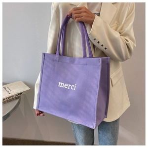 Dettaglio di una borsa tote in tela viola con testo merci bianco tenuta da modella