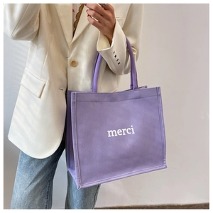 Dettaglio della borsa tote in tela viola con stampa merci bianca portata da una modella