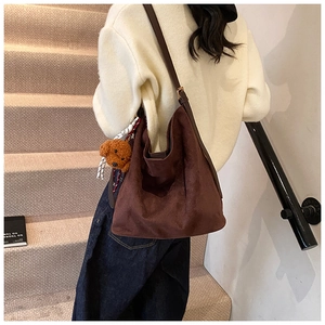 Detail of dark brown suede tote bag with plush bear charm worn by a model