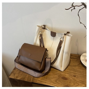 Brown leather crossbody bag with patterned strap and cream tote bag on wooden surface