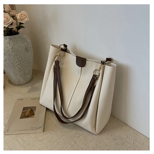 Detail of minimalist cream tote bag with dark brown straps and gold metal ring hardware